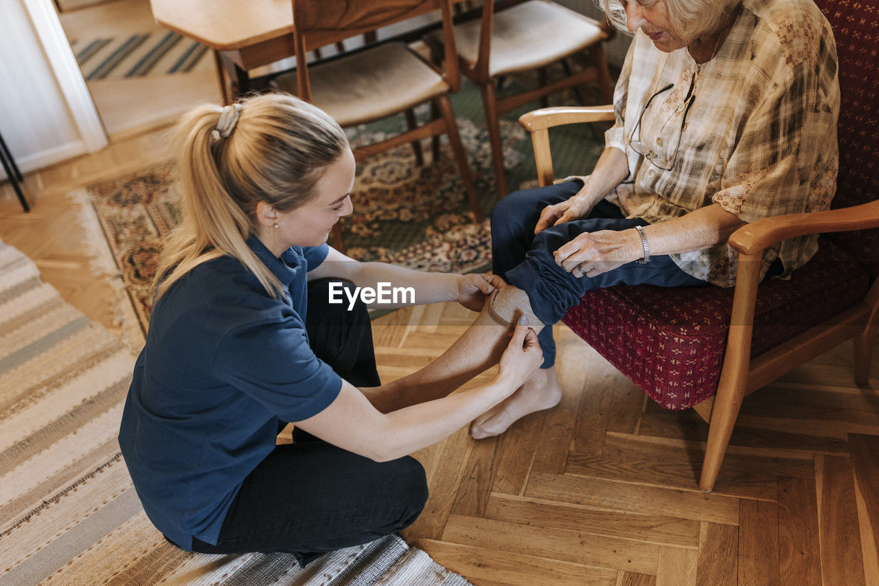 High angle view of female healthcare worker helping senior woman wearing socks at home