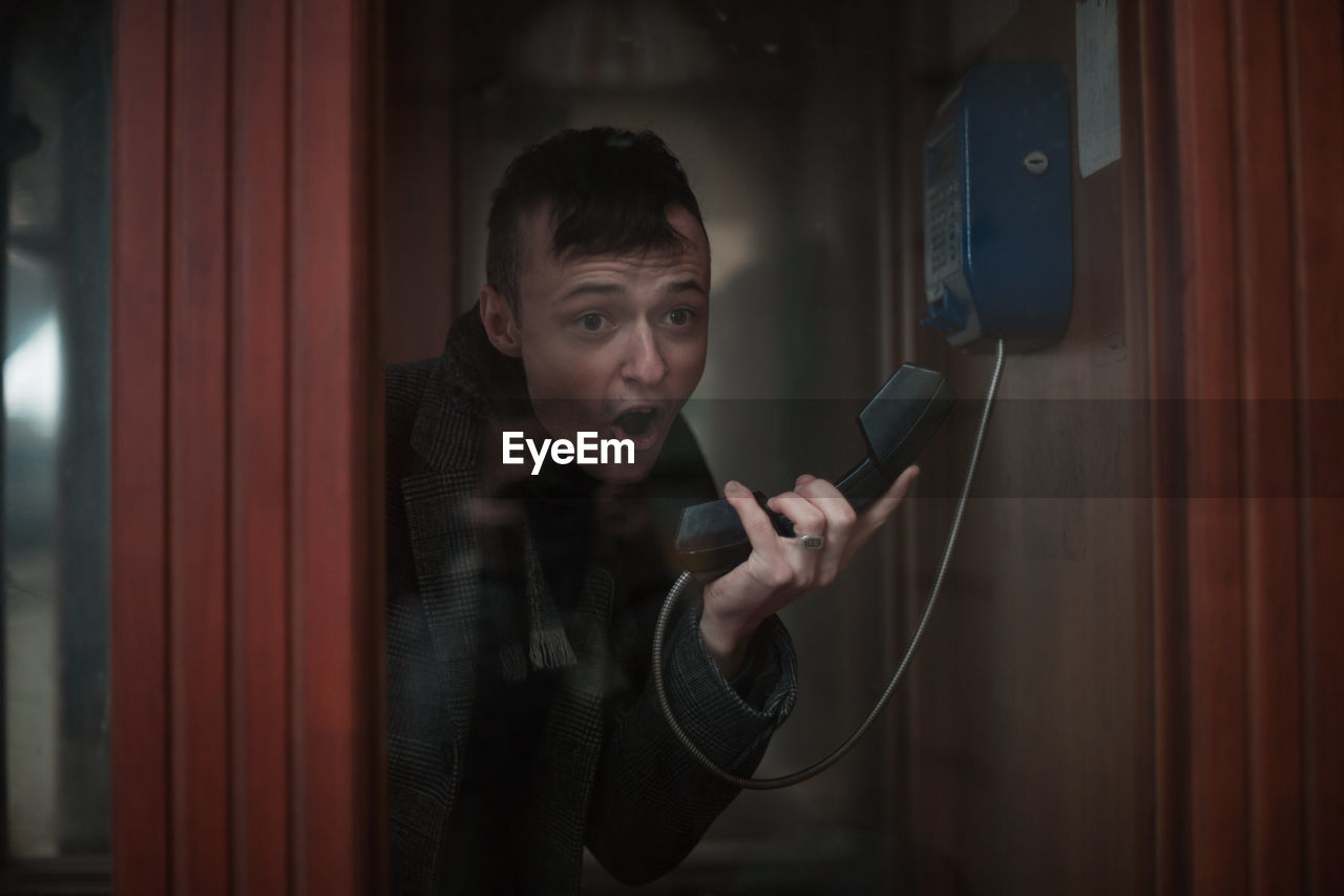 Young man talking on telephone seen through glass