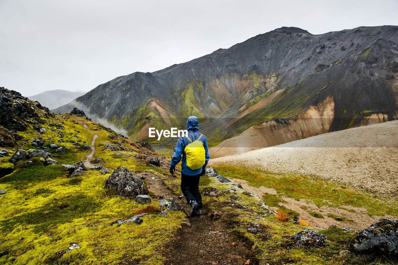 Rear view of man walking on mountain against sky