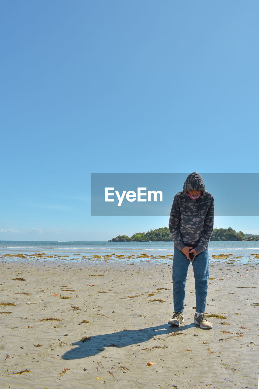 rear view of man standing at beach against clear sky