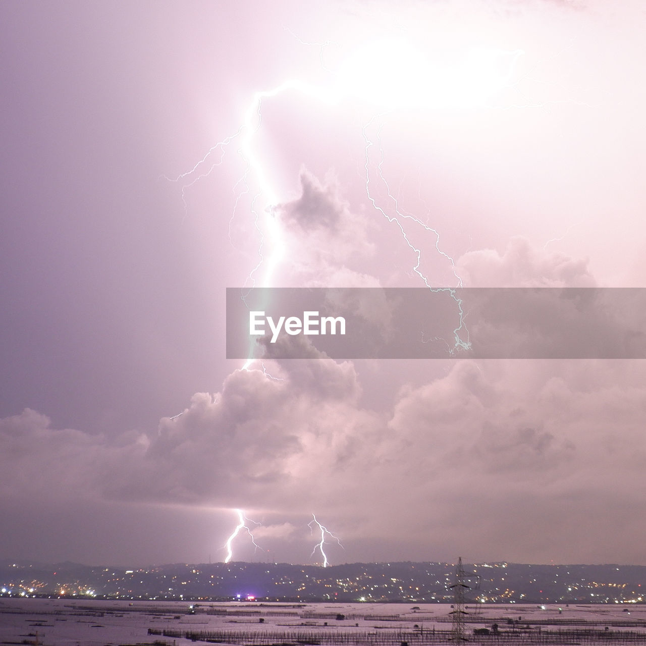 Lightning over illuminated cityscape against sky