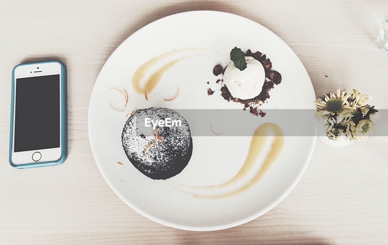 Directly above view of dessert in plate with mobile phone on table