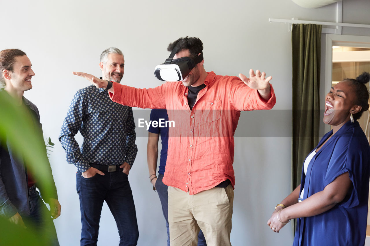 Happy business people looking at male colleague using virtual reality simulator in office