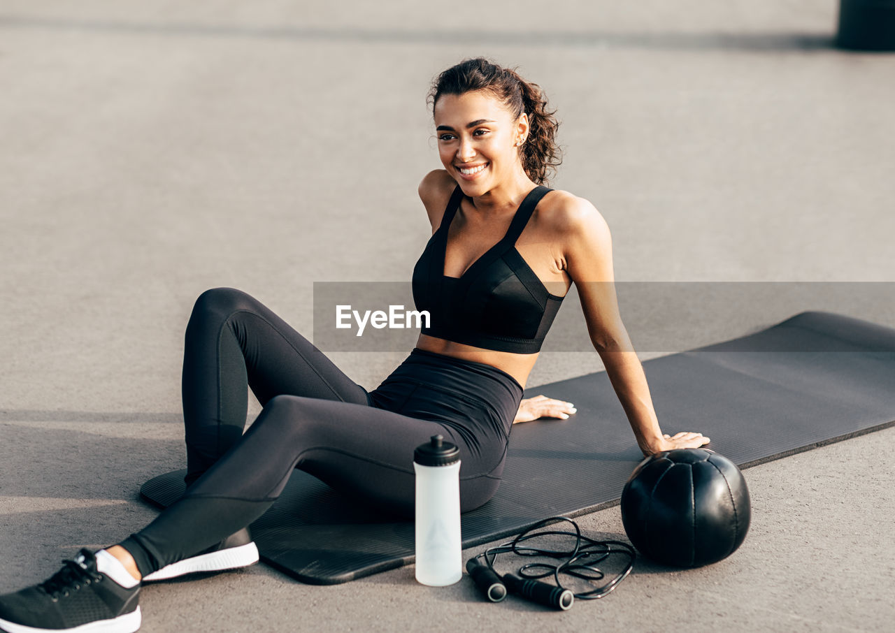 Smiling young woman sitting on exercise mat