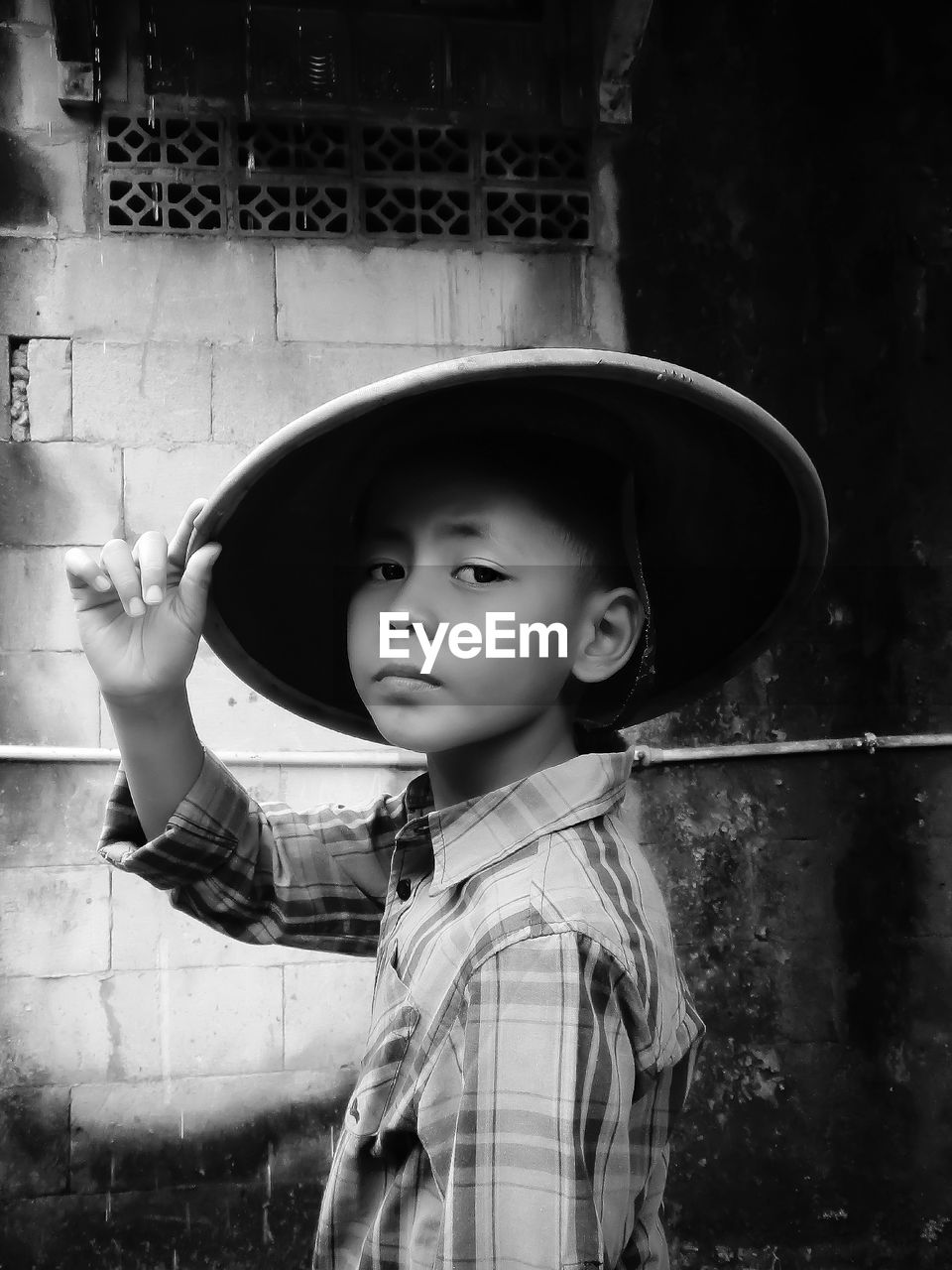 Rear view of man standing against wall, boy wearing a bamboo hat