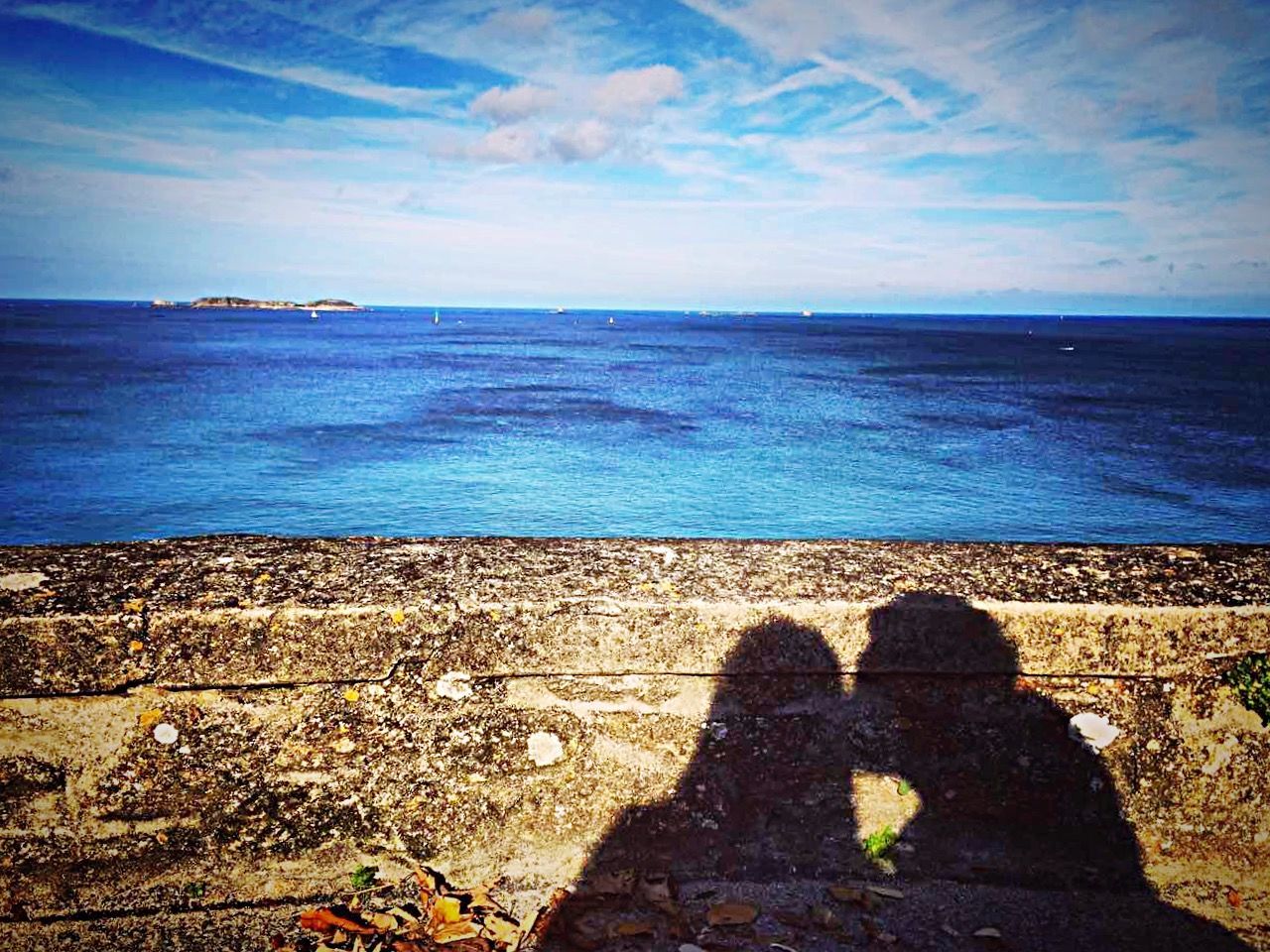 Shadow of man and woman on retaining wall by sea against sky