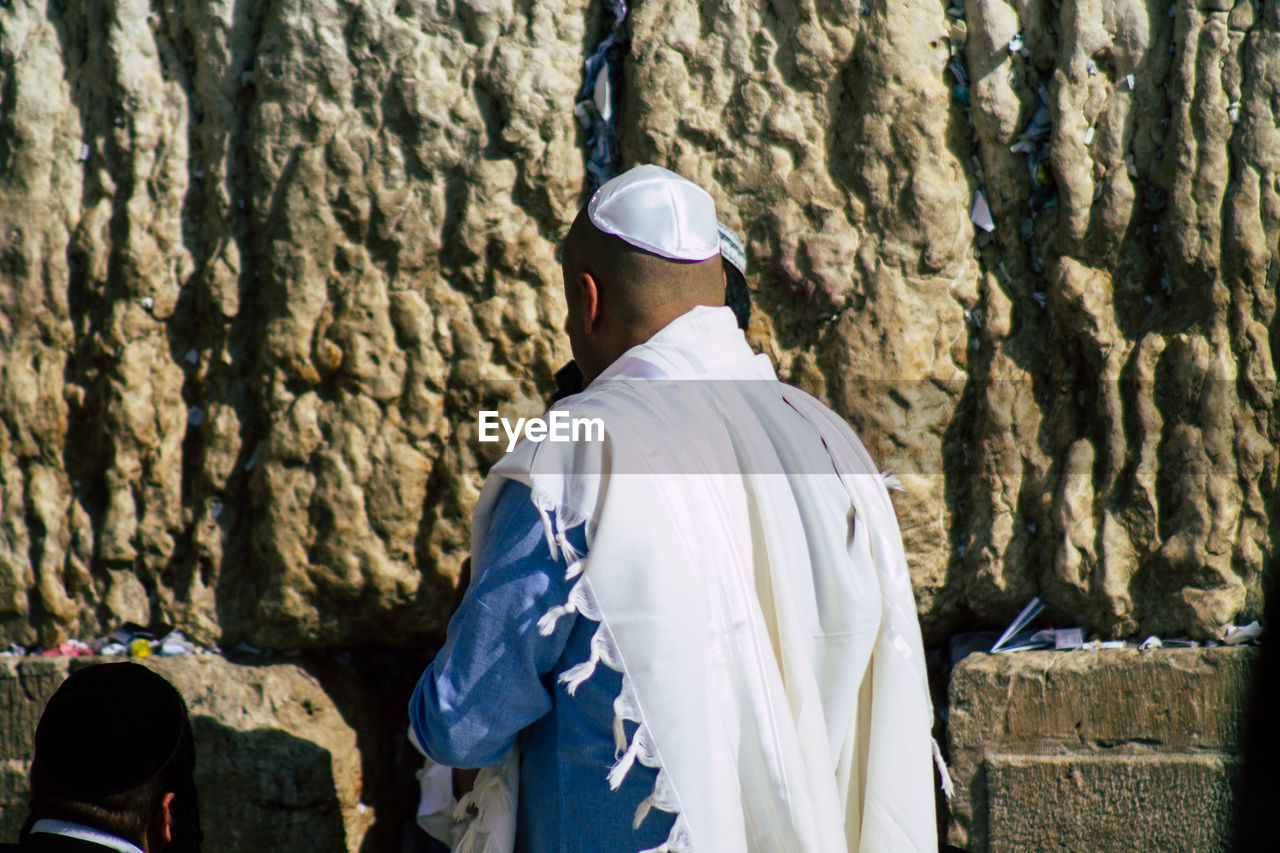 REAR VIEW OF MAN STANDING AT TEMPLE AGAINST TREE