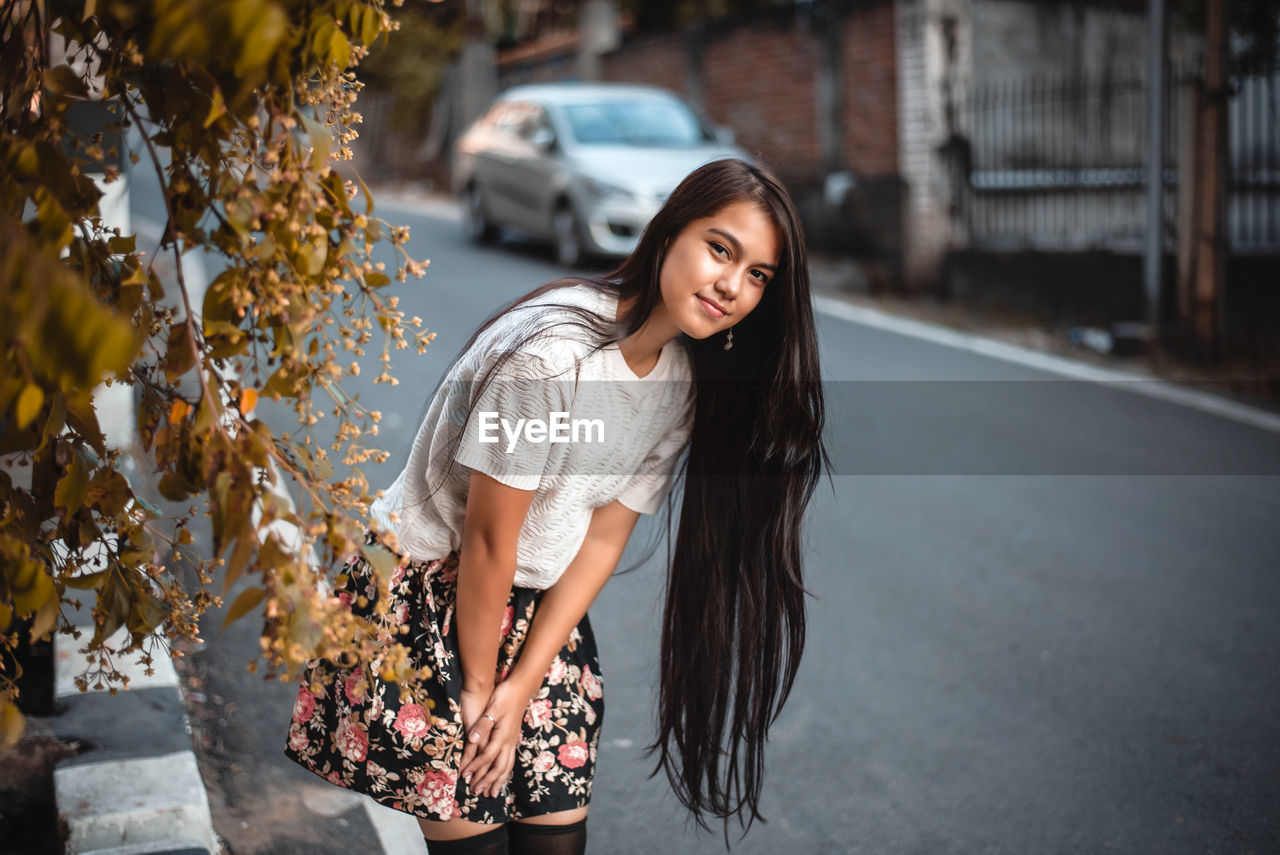 PORTRAIT OF YOUNG WOMAN STANDING AGAINST TREE