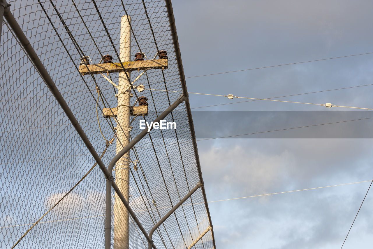 Low angle view of chainlink fence by telephone pole against cloudy sky