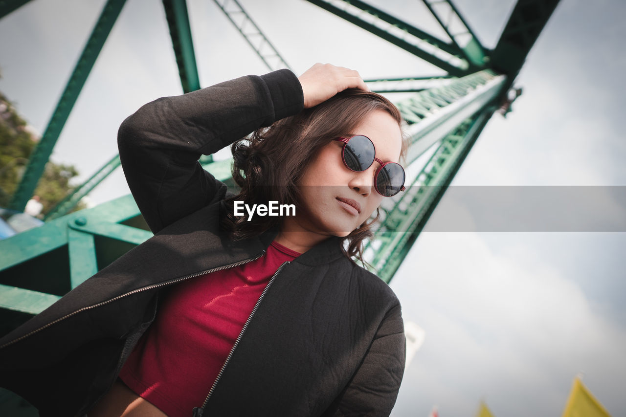 Woman wearing sunglasses against metallic structure and sky