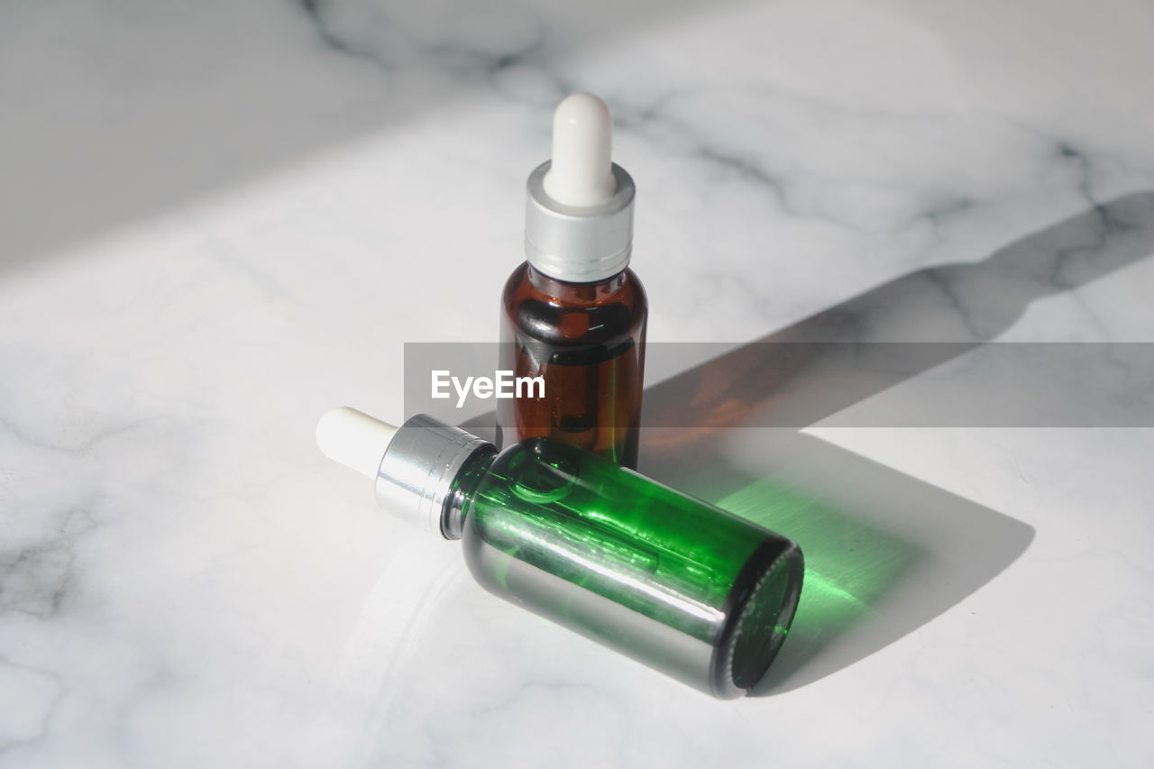 Green and brown bottle facial essential oil or serum packaging on white marble background. 