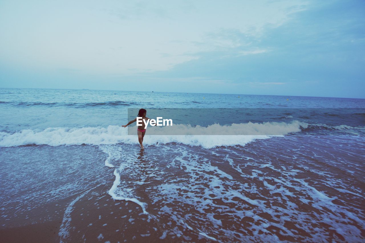 Shirtless girl wading in sea against sky