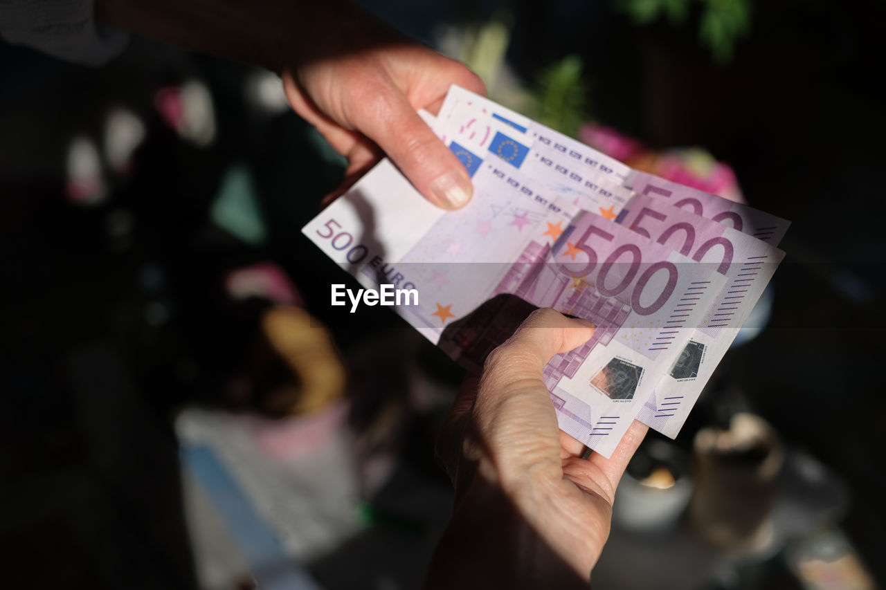 Close-up of two female hands handing over 500 euro notes 