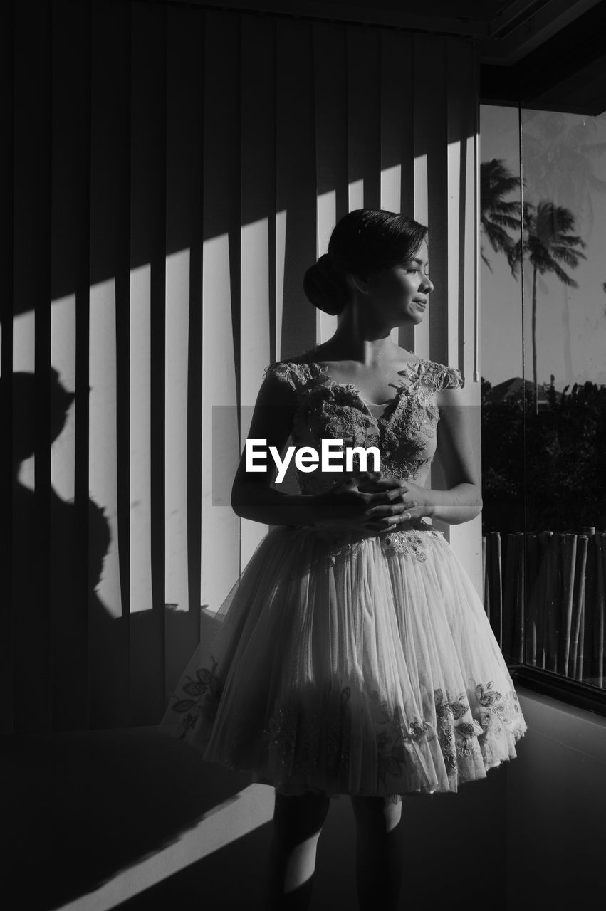 YOUNG WOMAN LOOKING AWAY WHILE STANDING IN ROOM