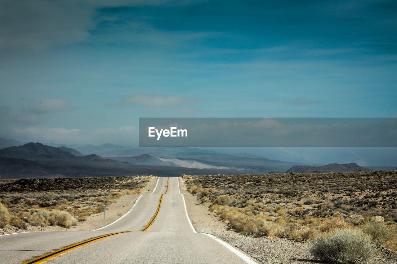 Empty road amidst landscape against sky