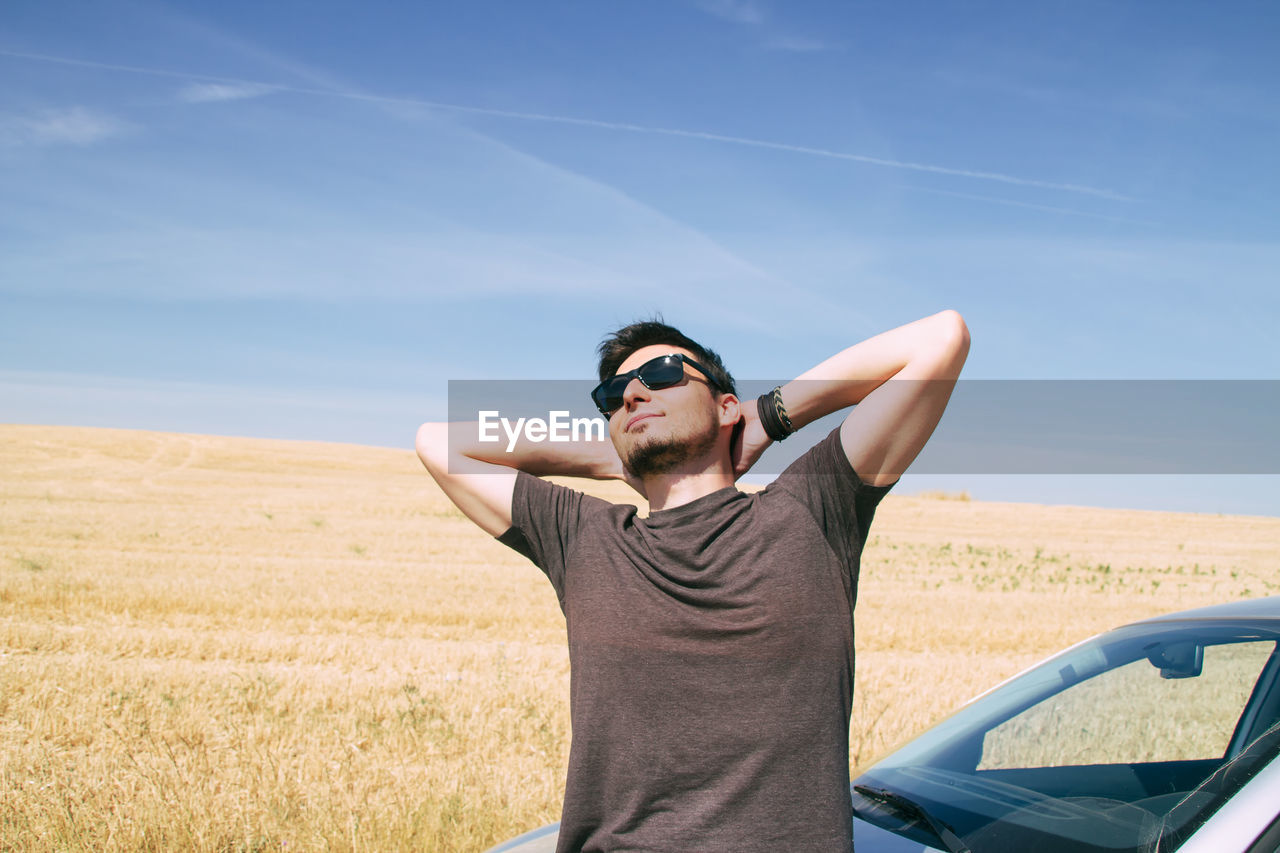 Smiling man wearing sunglasses while leaning on car against sky