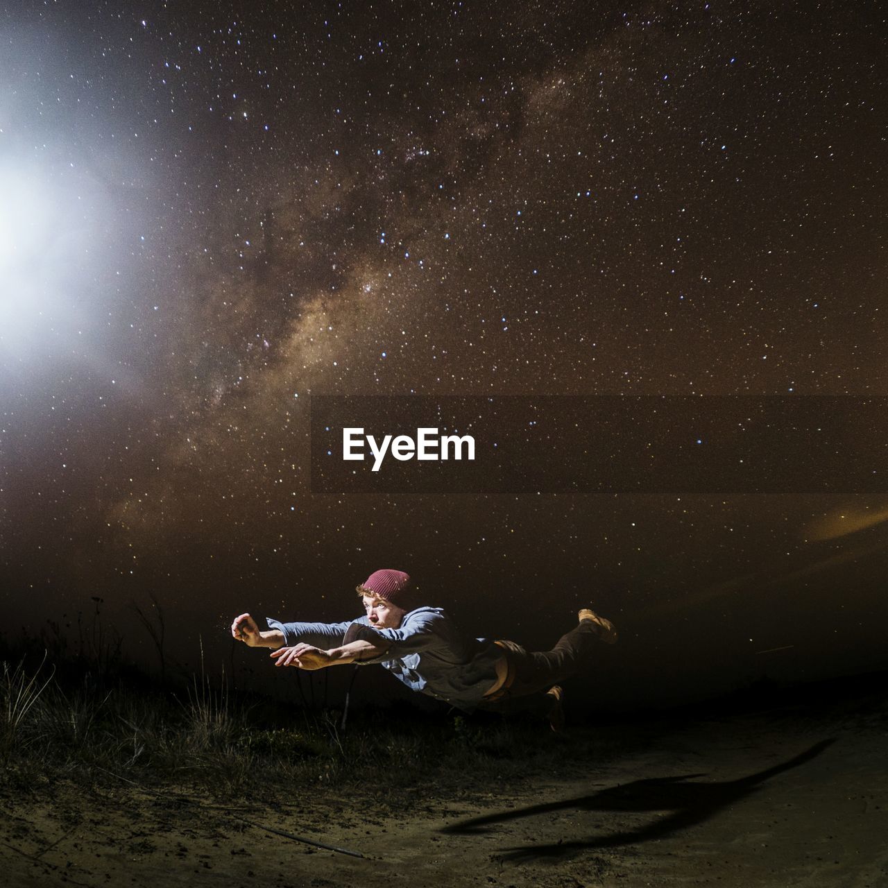 Young man levitating above field at night