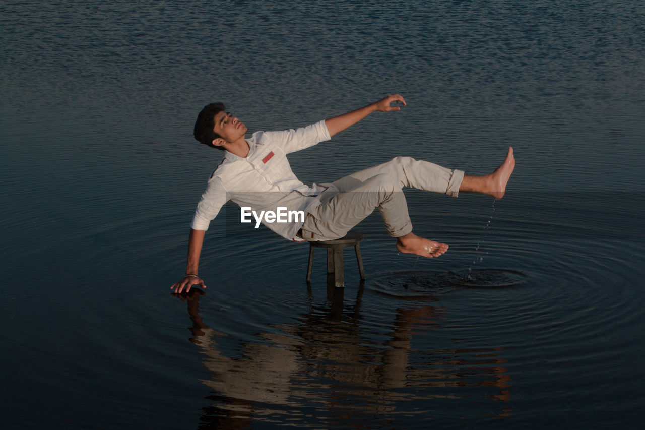 Full length of young man balancing on stool amidst lake
