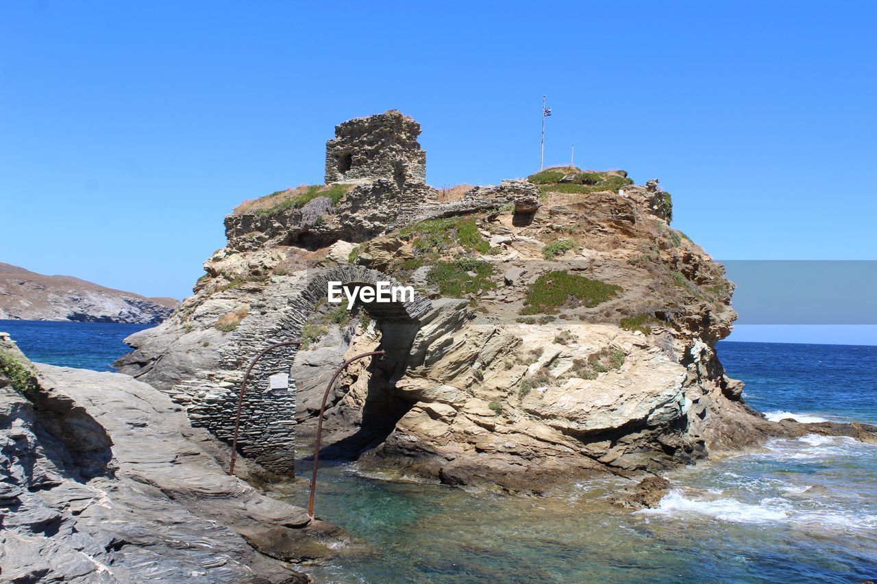 Rock formations in sea against clear blue sky