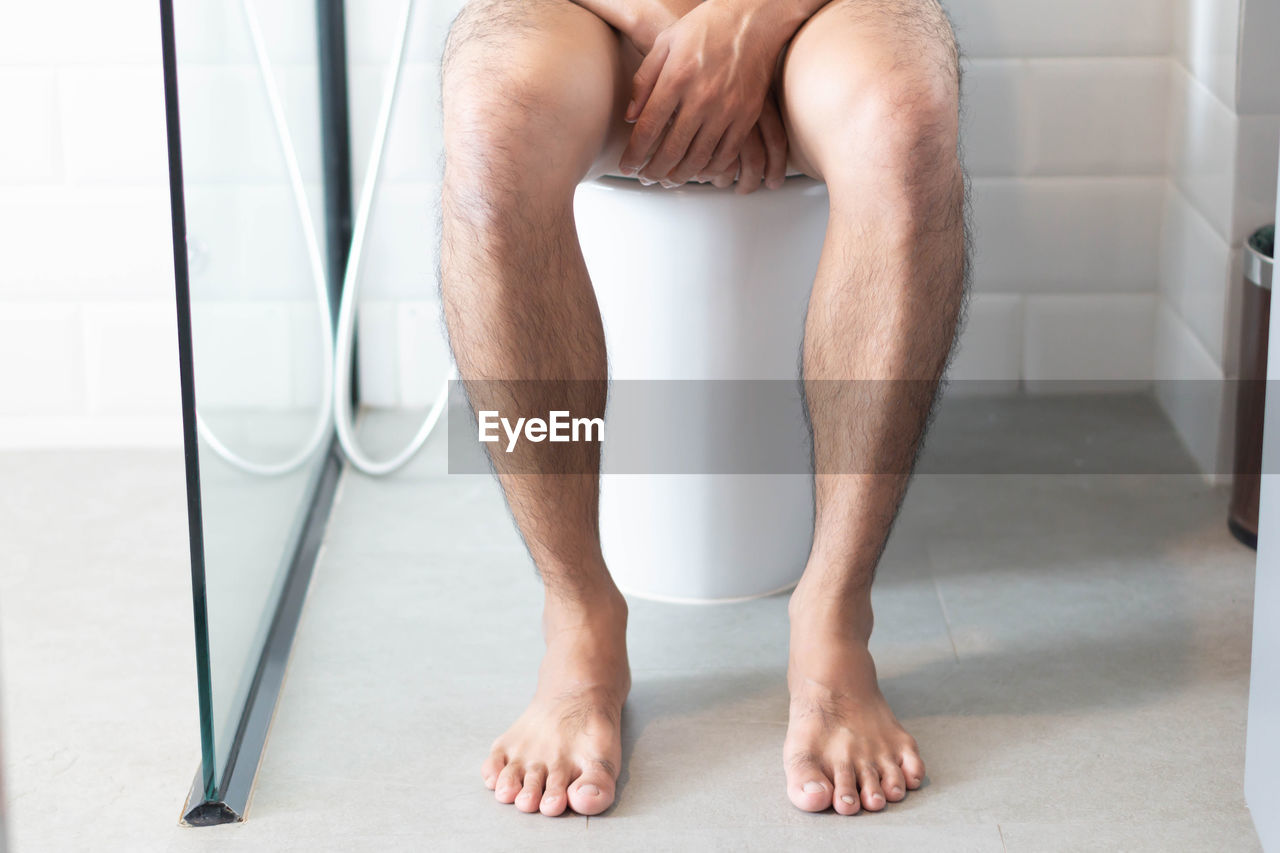 Low section of man sitting on toilet bowl