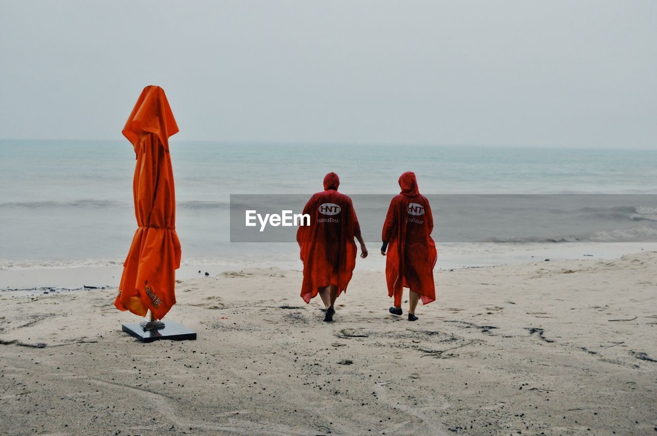 REAR VIEW OF PEOPLE ON BEACH AGAINST SKY