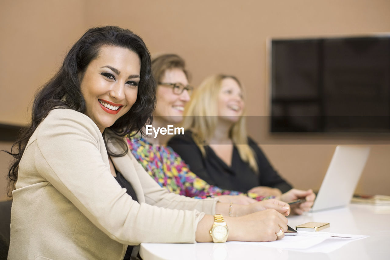 Portrait of happy businesswoman with colleagues sitting at conference table in creative office