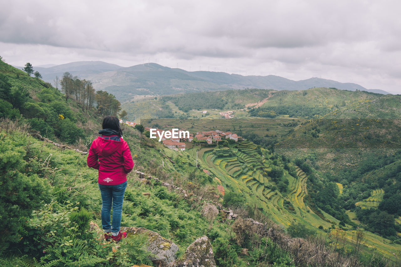 Rear view of woman standing on mountain against cloudy sky