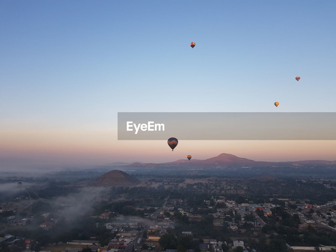 Hot air balloons flying in city against sky during sunrise