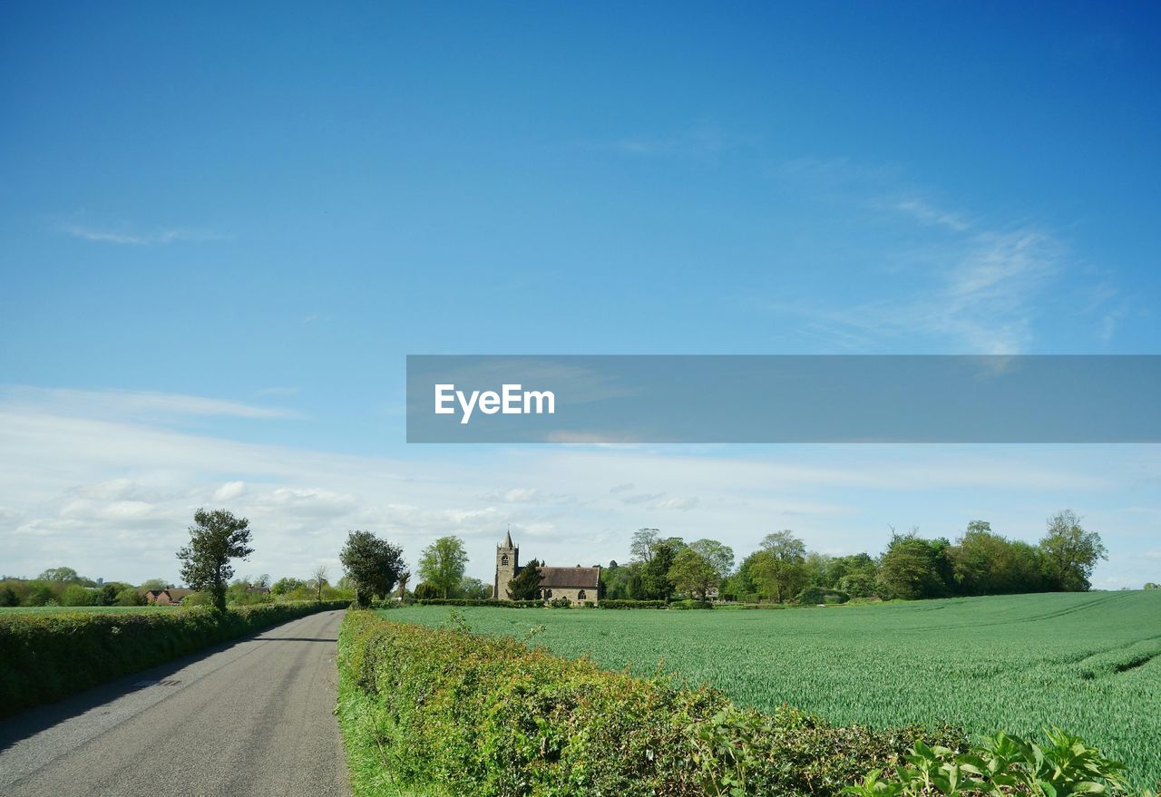 Road by grassy field against blue sky