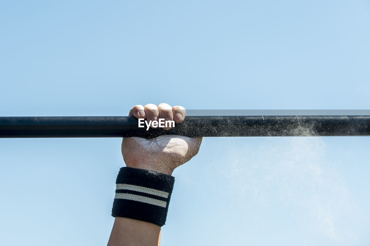 Cropped hand of woman holding rod against clear sky