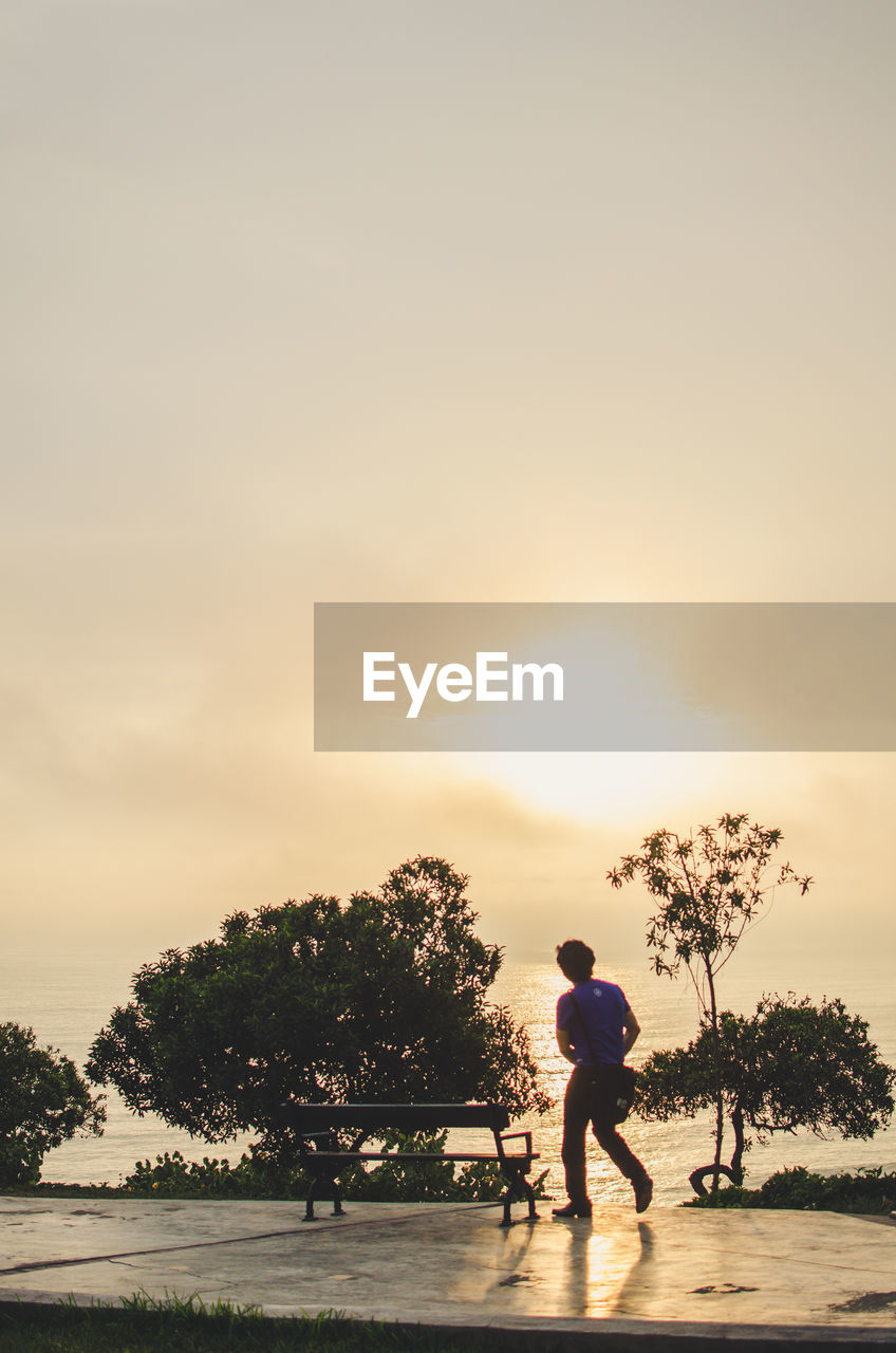 Man walking at beach against sky during sunset