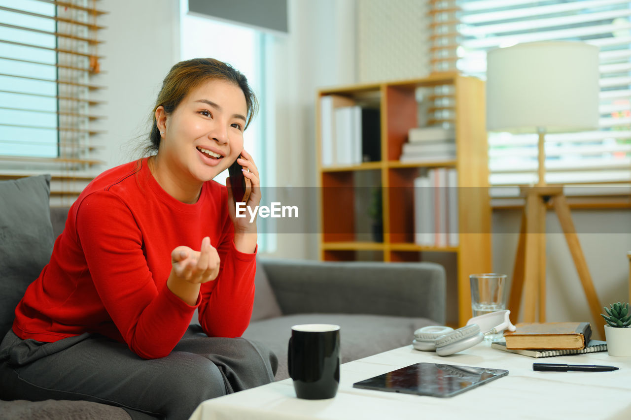 portrait of young woman using phone while sitting on table