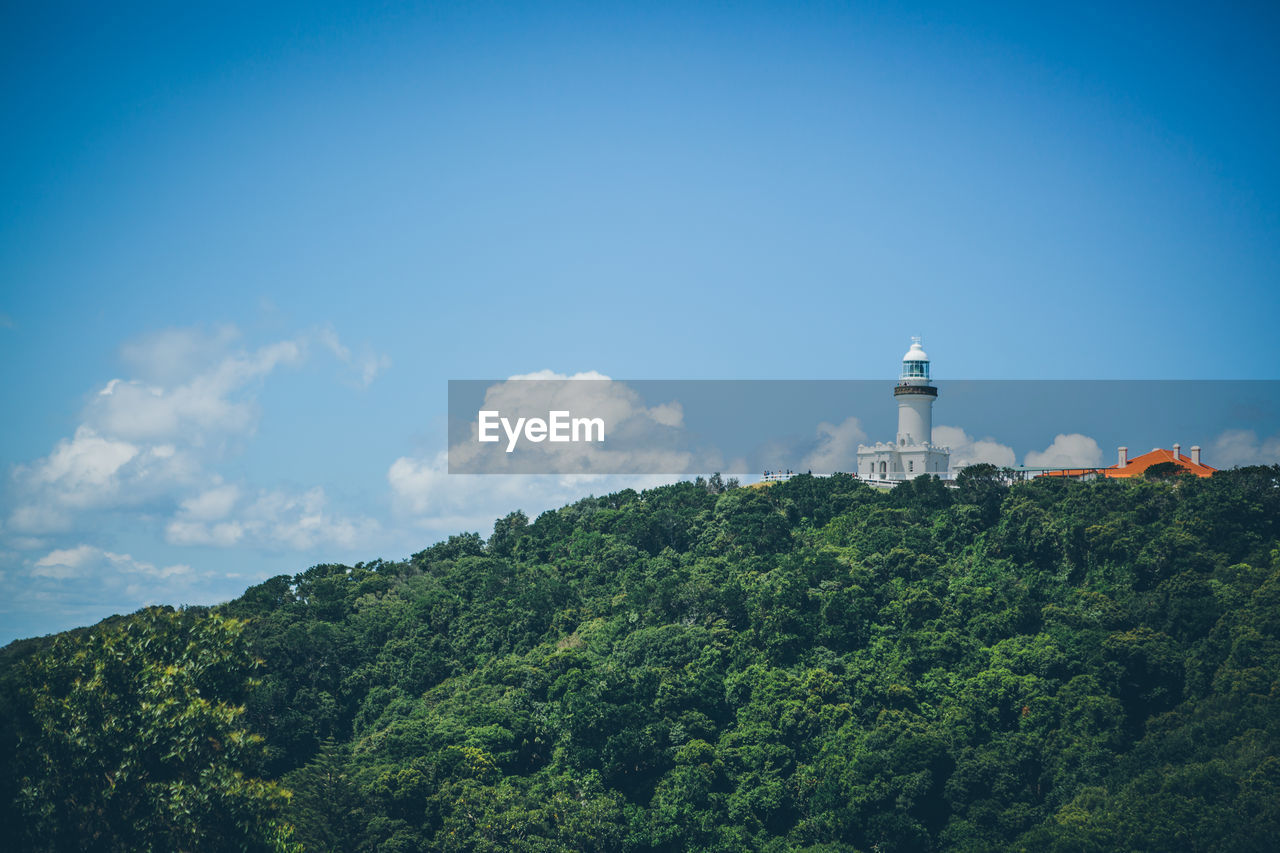 Trees and lighthouse against cloudy sky