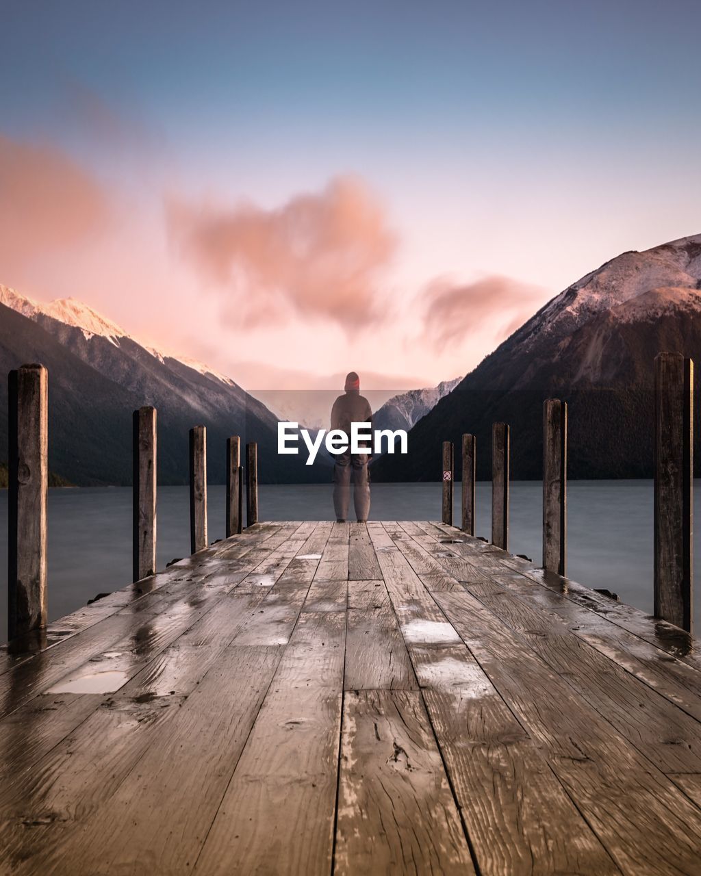 Rear view of woman standing on pier over lake against sky during sunset