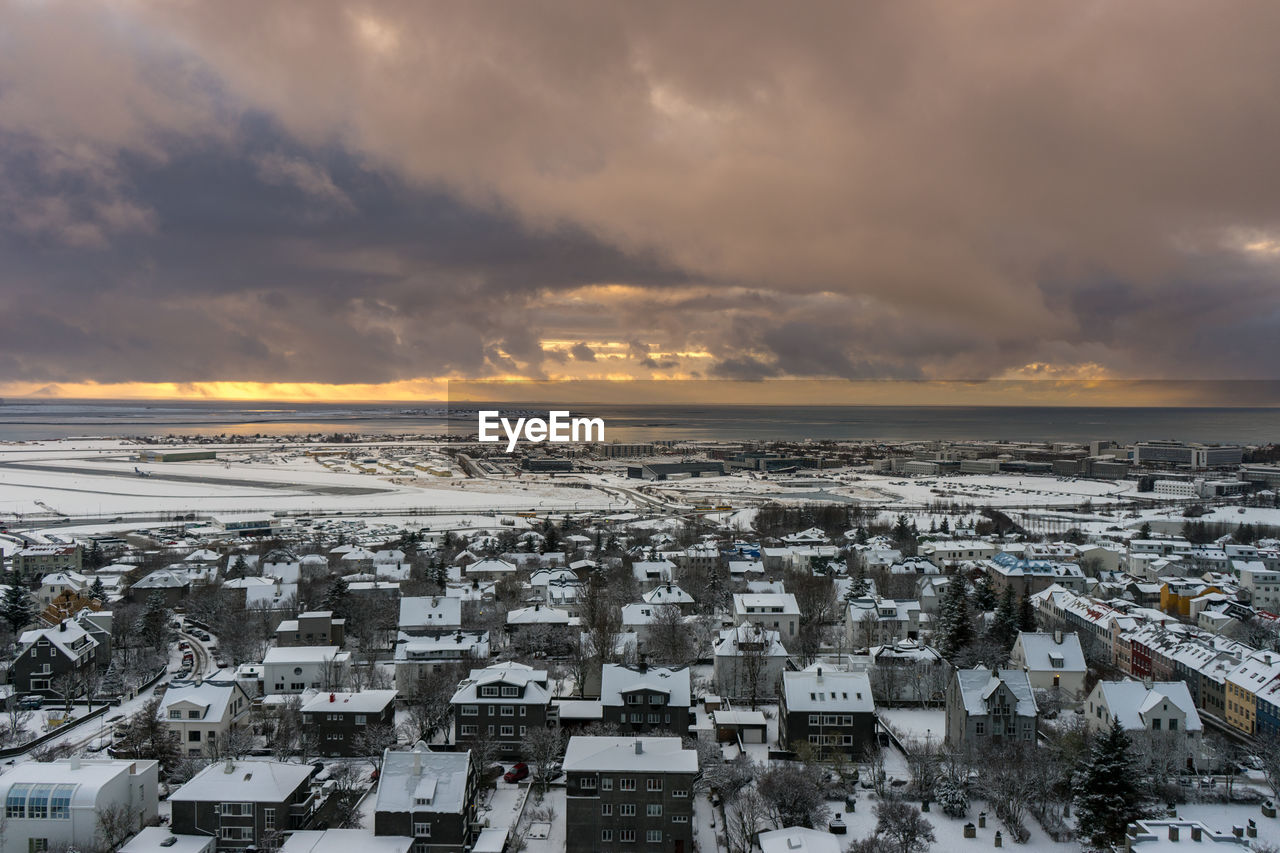 Aerial view of townscape against cloudy sky during winter at sunset