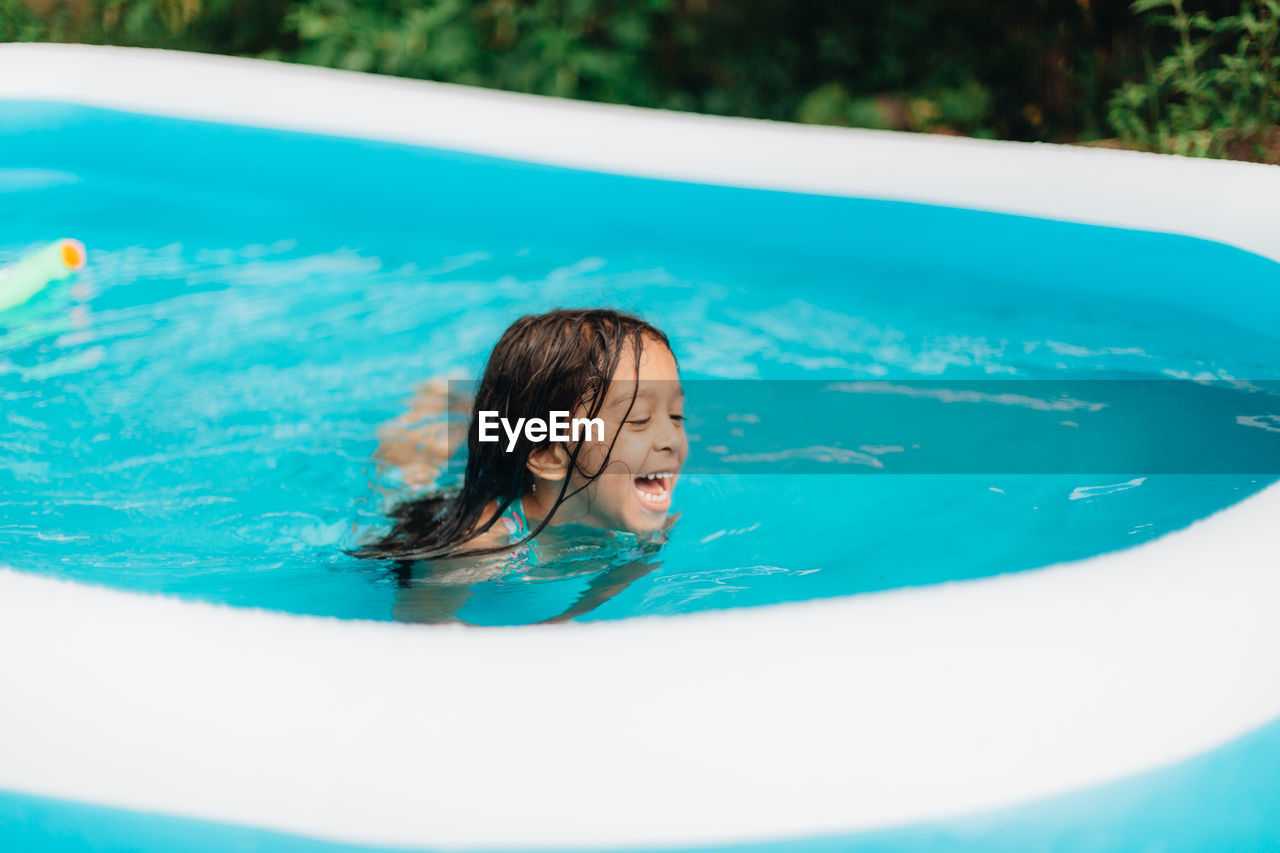 Diverse mixed race toddler girl at home having fun in kiddie pool in backyard being very happy