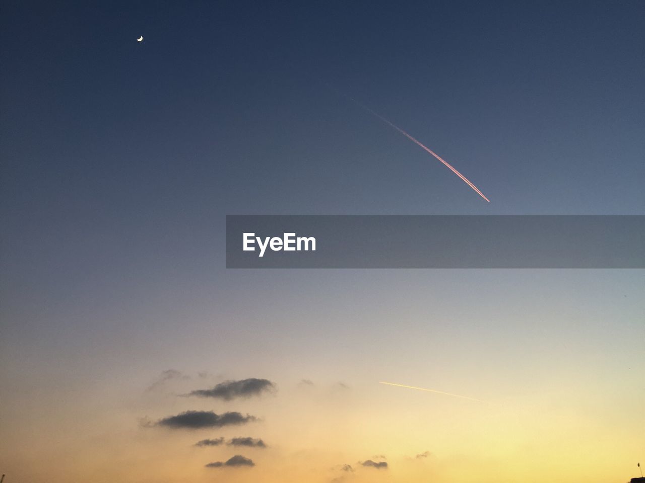 Low angle view of vapor trail and moon against sky at dusk