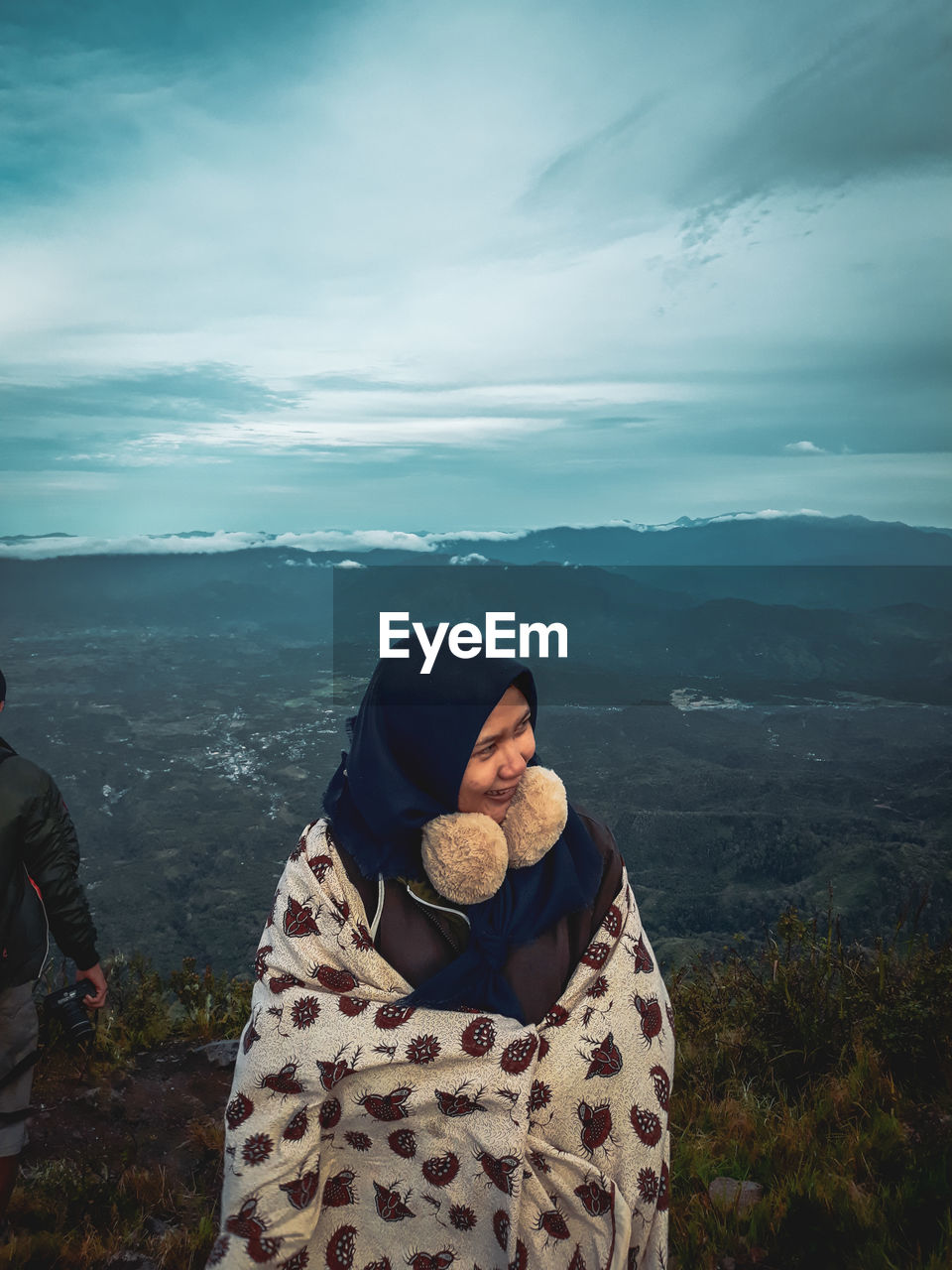 Woman wrapped in blanket looking away while standing against mountains