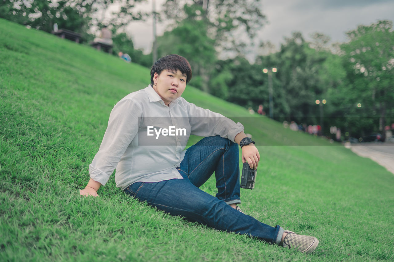 Portrait of young woman with camera sitting on grassy land in park