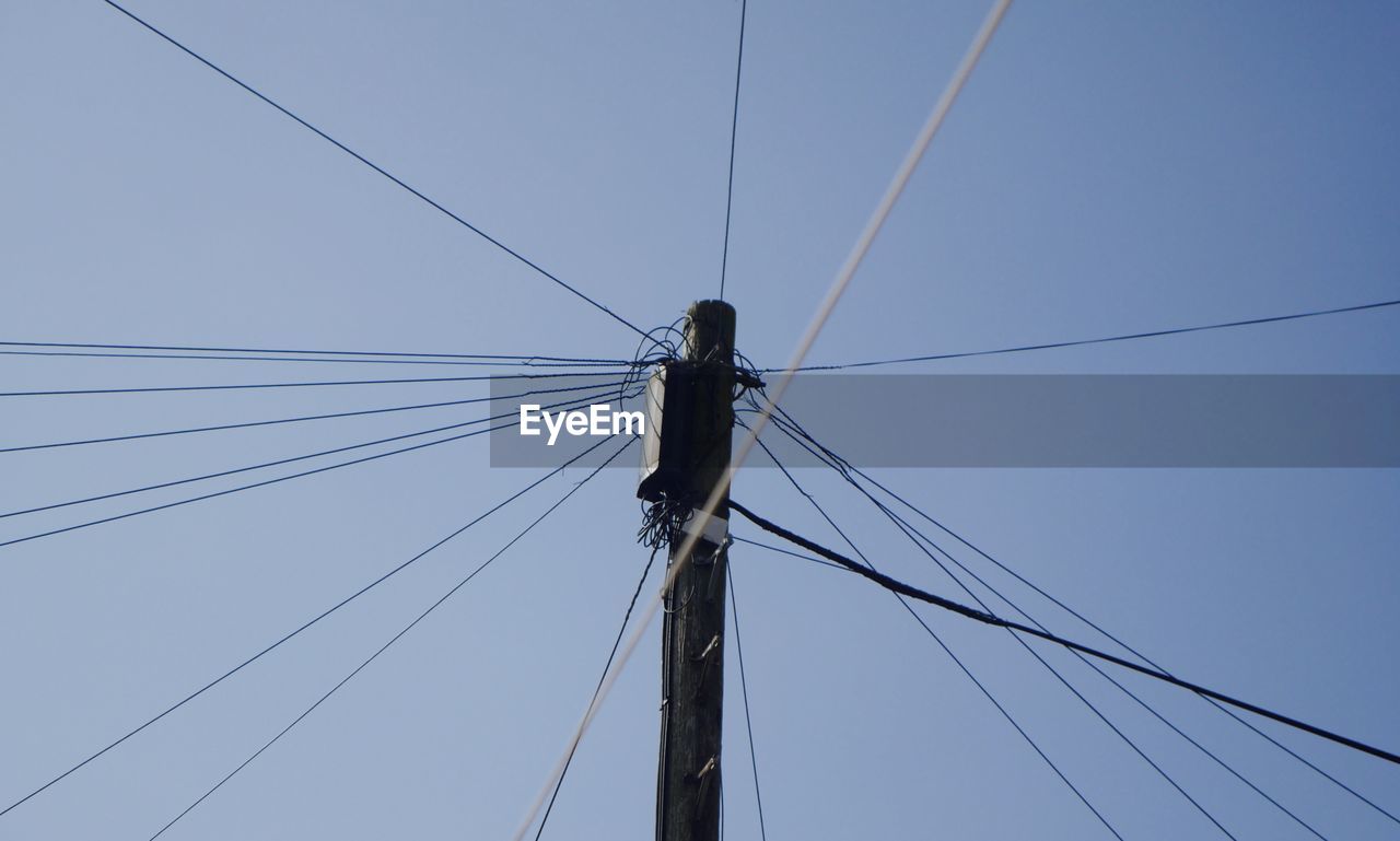 Low angle view of cables connected to electricity pylon against clear sky