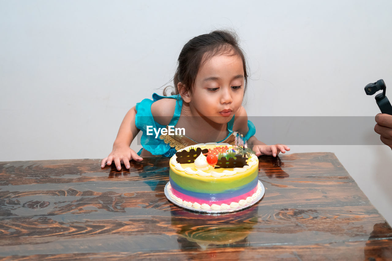 Little girl is blowing candles on her birthday cake. celebrating at home during quarantine.