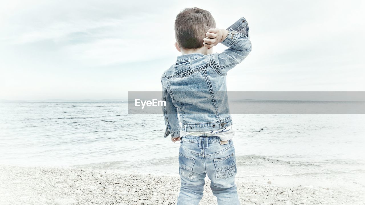 Rear view of boy standing on shore at beach