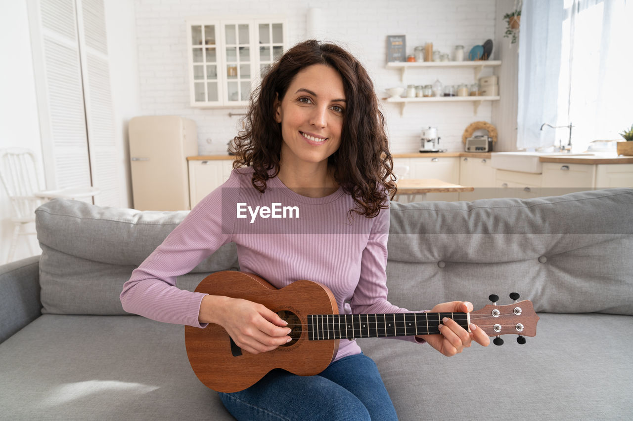 Portrait of smiling woman playing ukulele at home