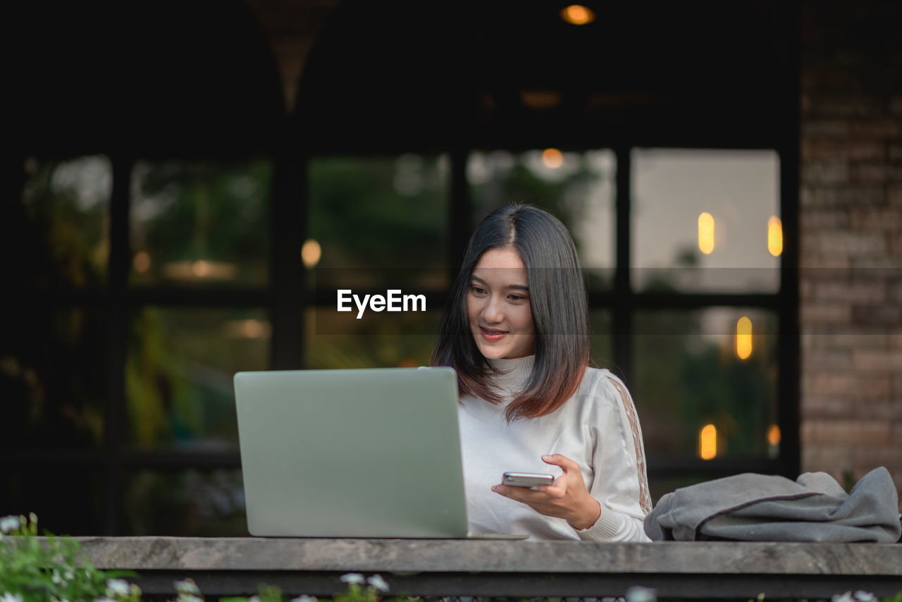 WOMAN LOOKING AT CAMERA WHILE SITTING ON TABLE