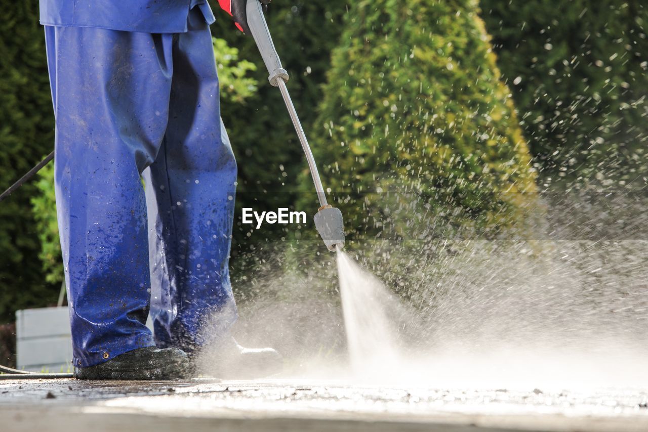 Low section of worker washing footpath