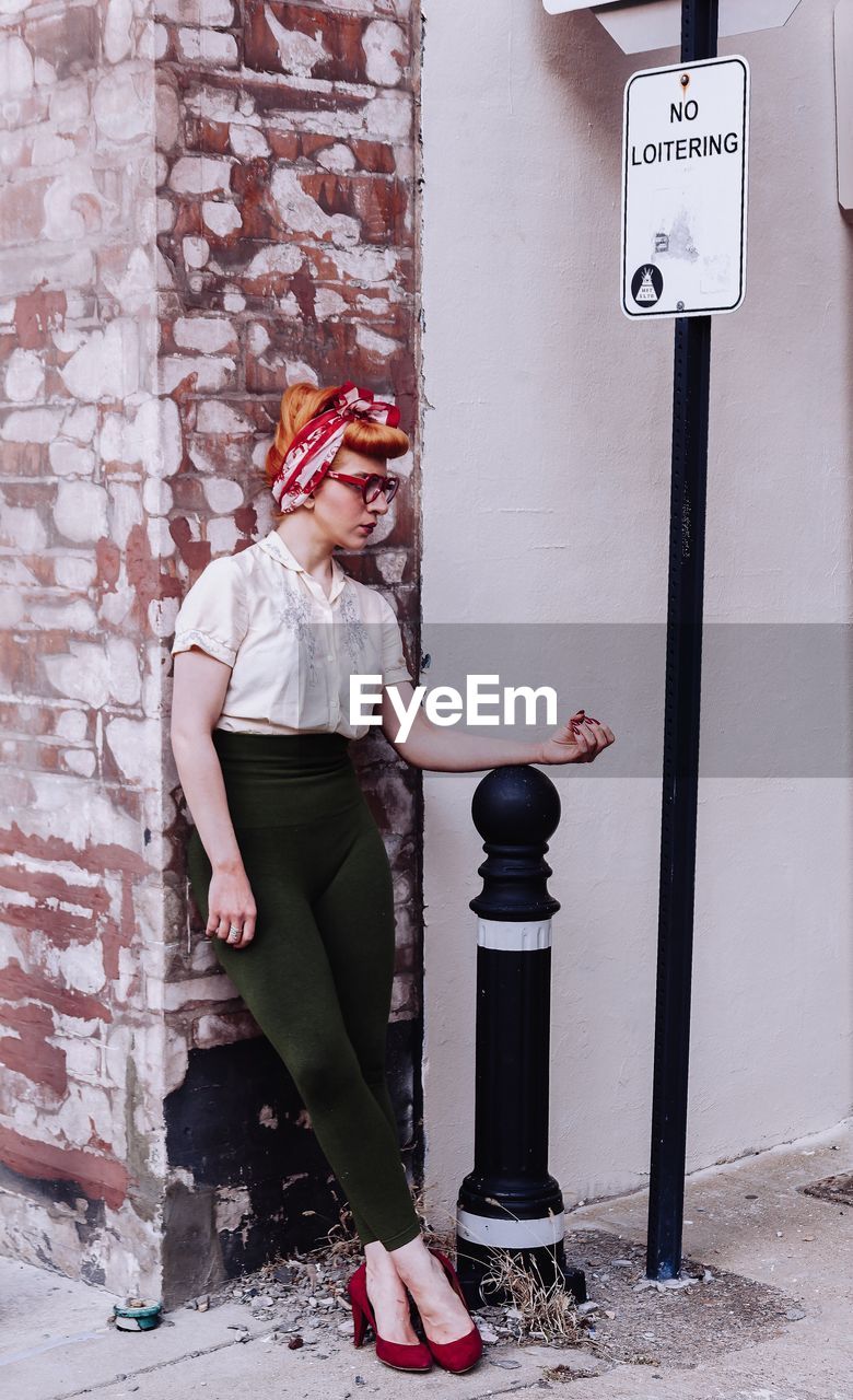 Beautiful woman standing on bollard on footpath at city