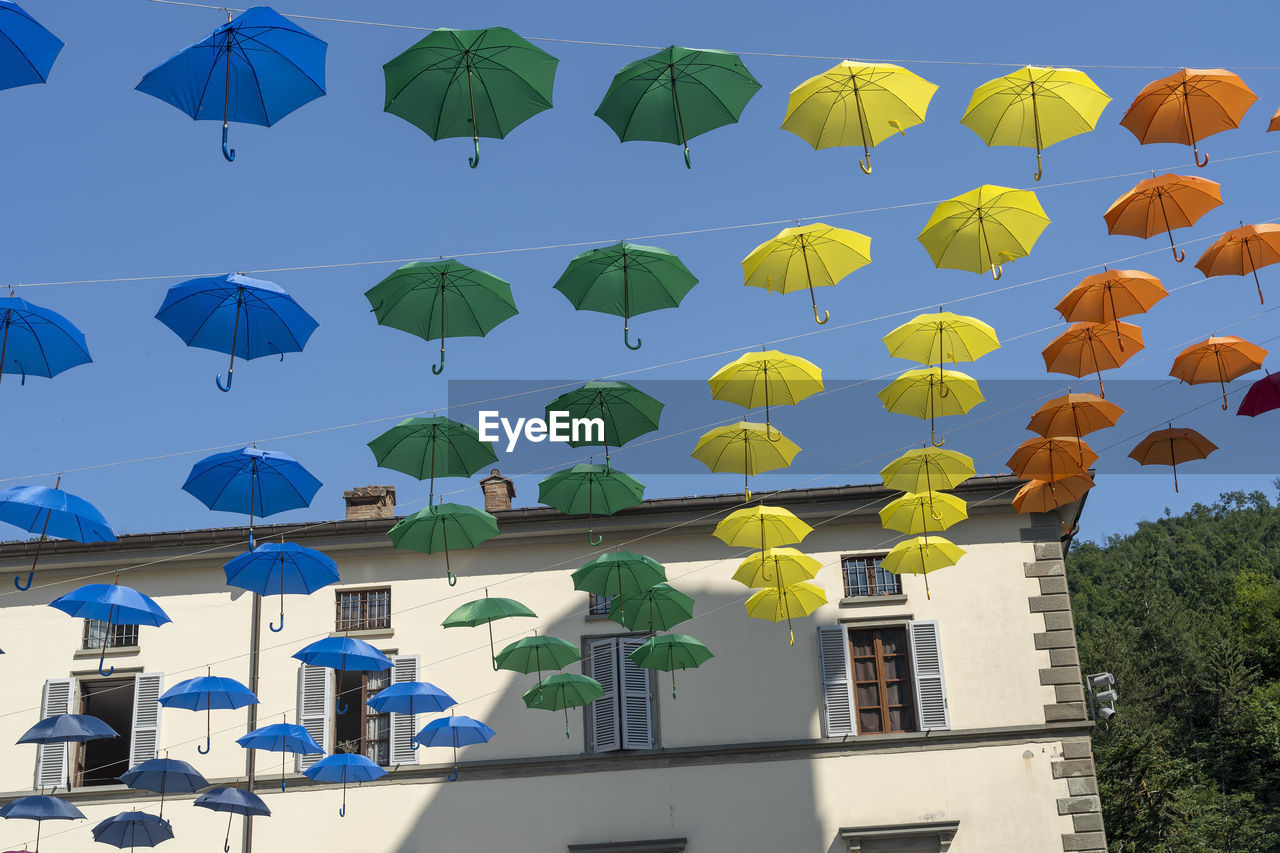 LOW ANGLE VIEW OF MULTI COLORED UMBRELLAS HANGING AGAINST BUILDING