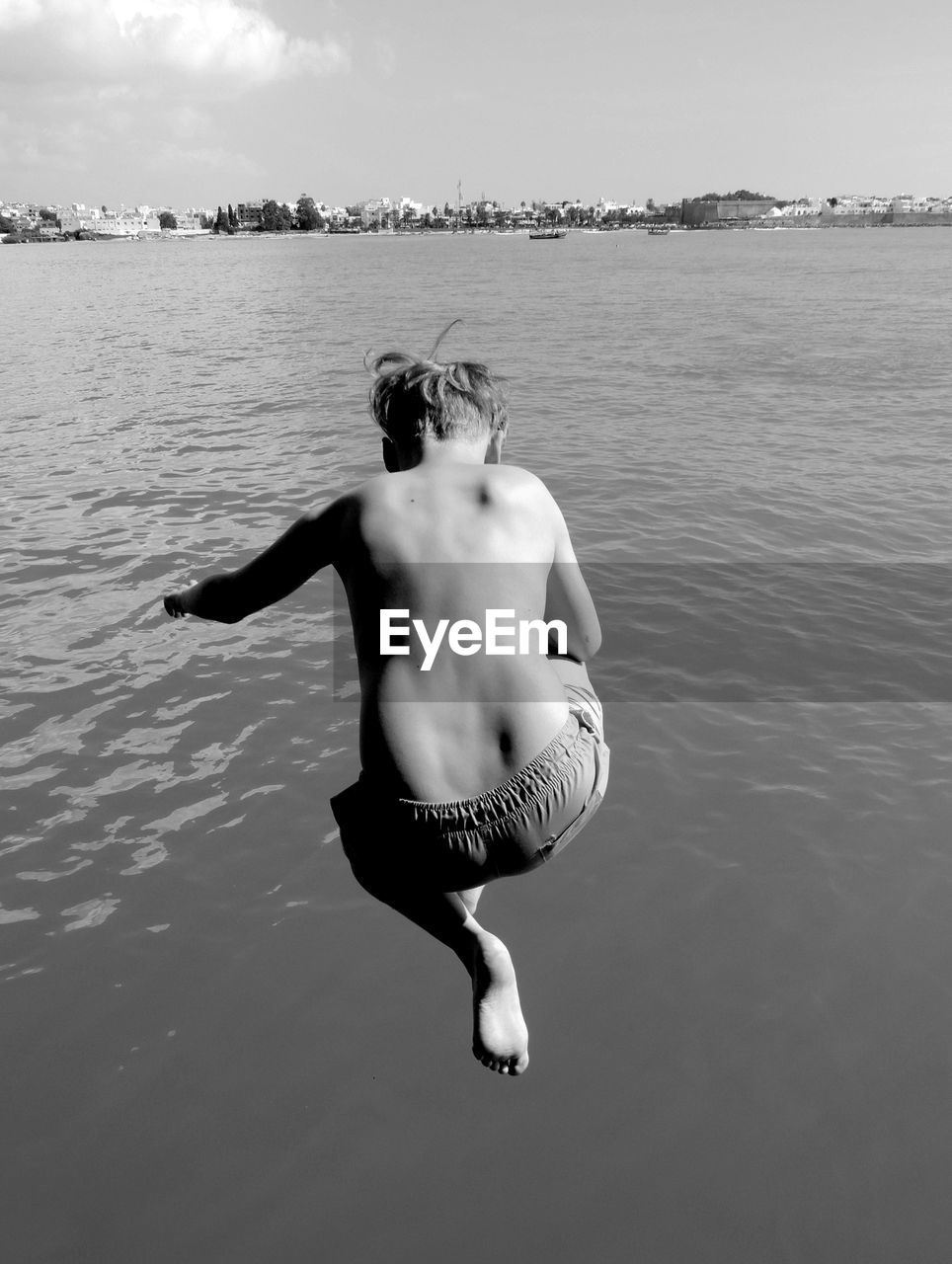 Rear view of shirtless boy jumping in lake against sky