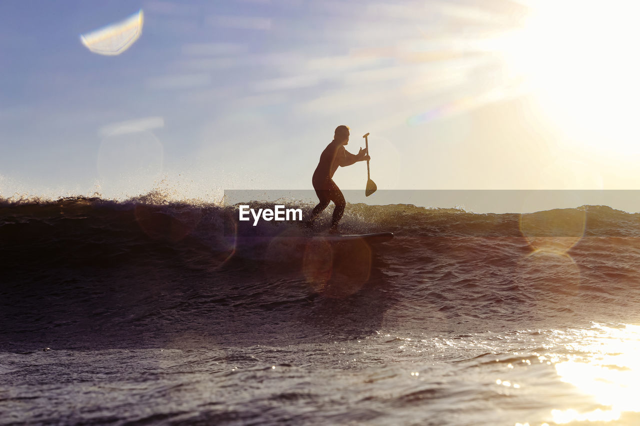 Male sup surfer at sunset time