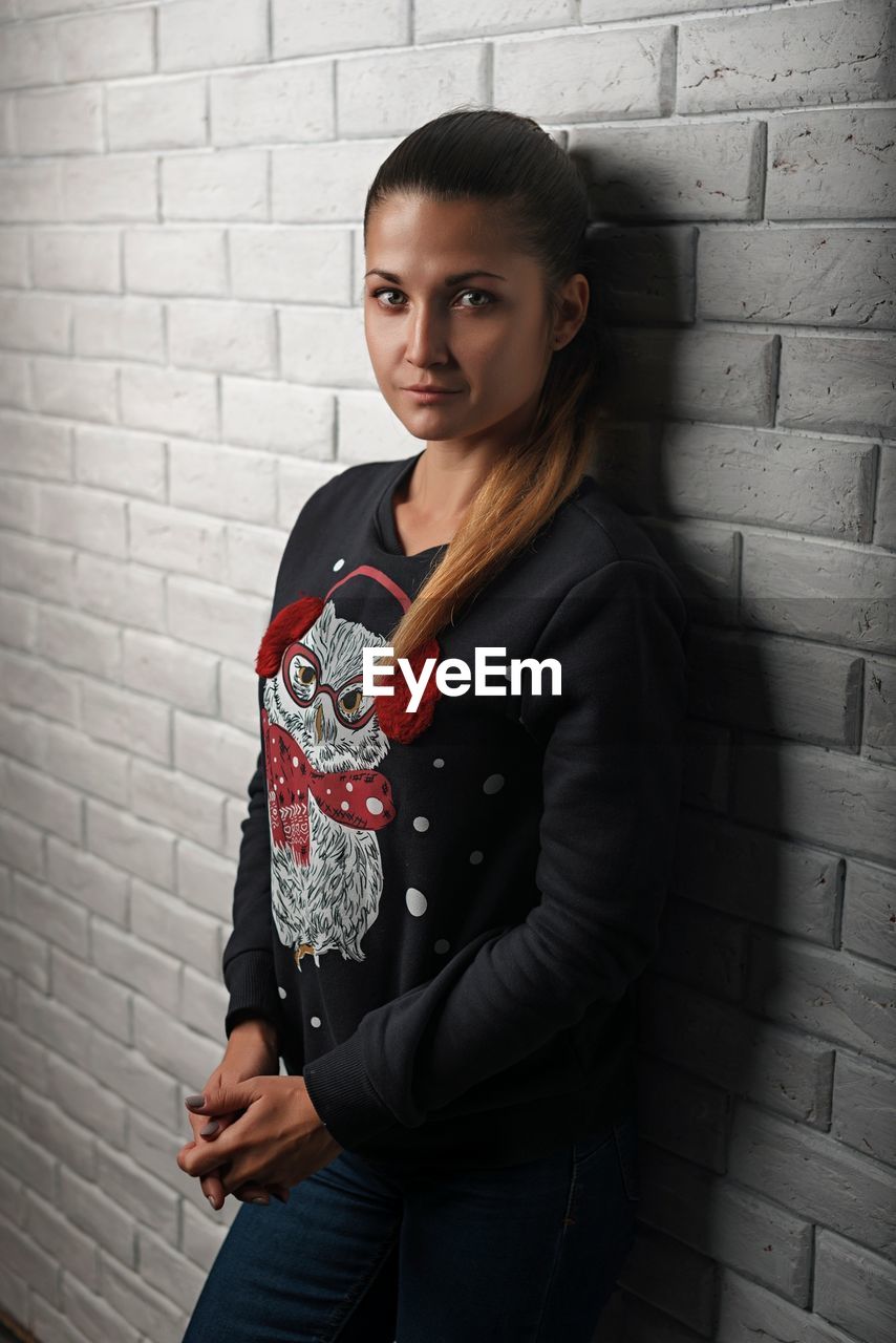 PORTRAIT OF A BEAUTIFUL YOUNG WOMAN STANDING AGAINST WALL